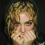 Person with wet hair wearing a dark hoodie, holding hands near face.