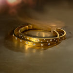 Two gold cuff bracelets with celestial star designs and cubic zirconia, resting on a golden satin surface.