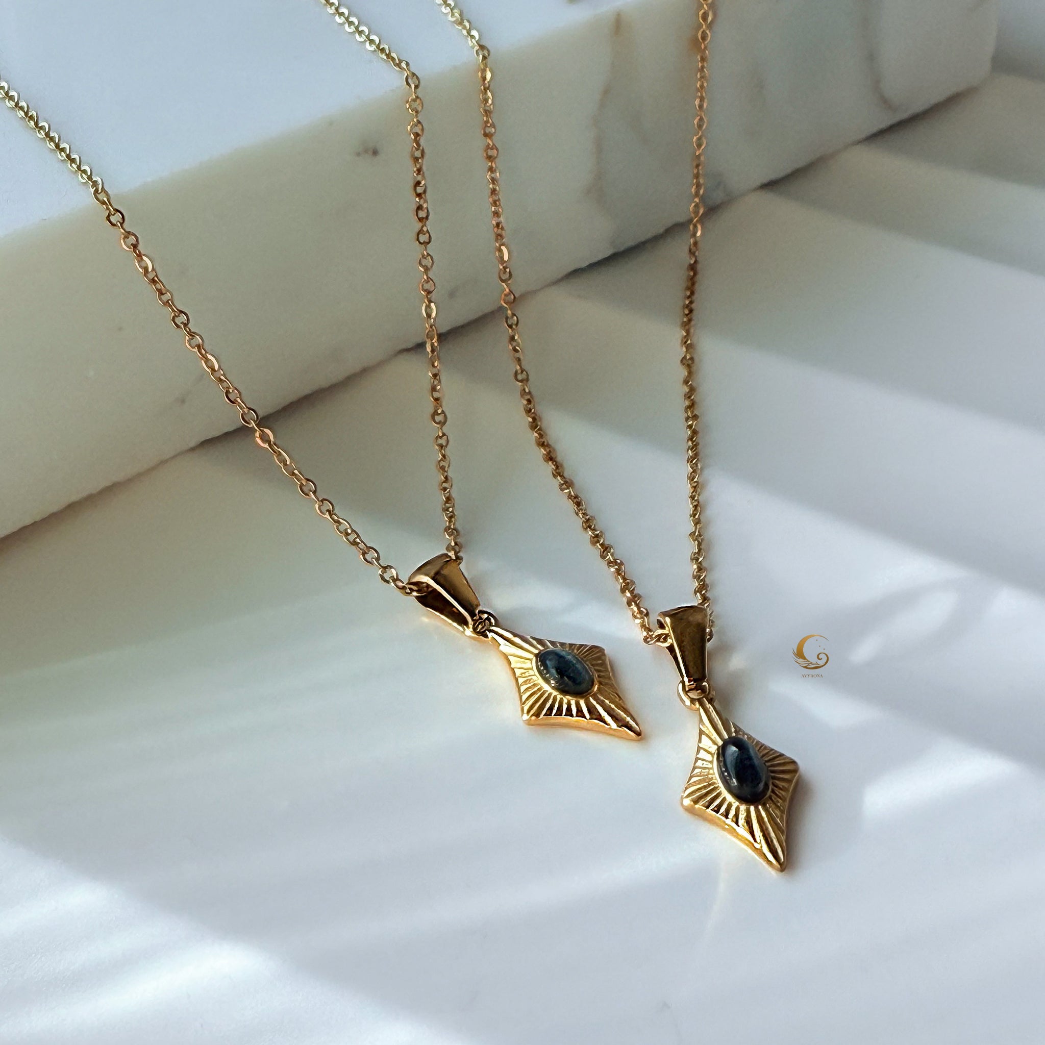 Gold necklaces with small black cat eye gemstone pendants in vintage-inspired settings, displayed on white marble background.