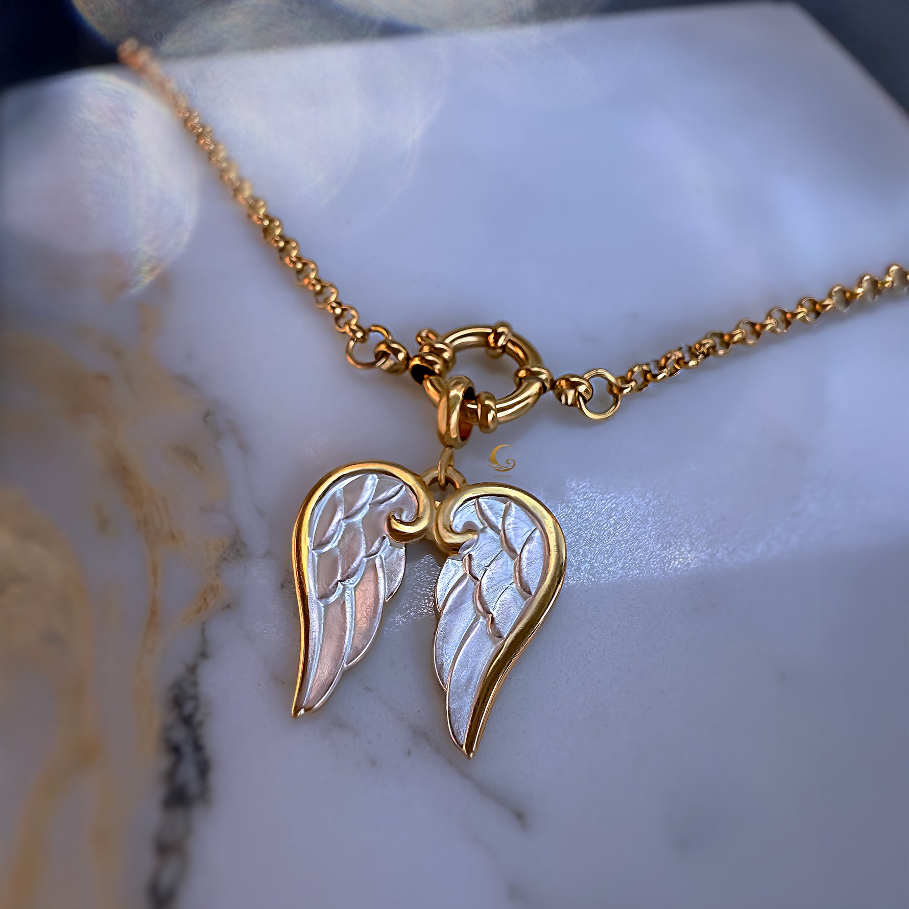 Gold necklace with angel wing pendant on a marble surface