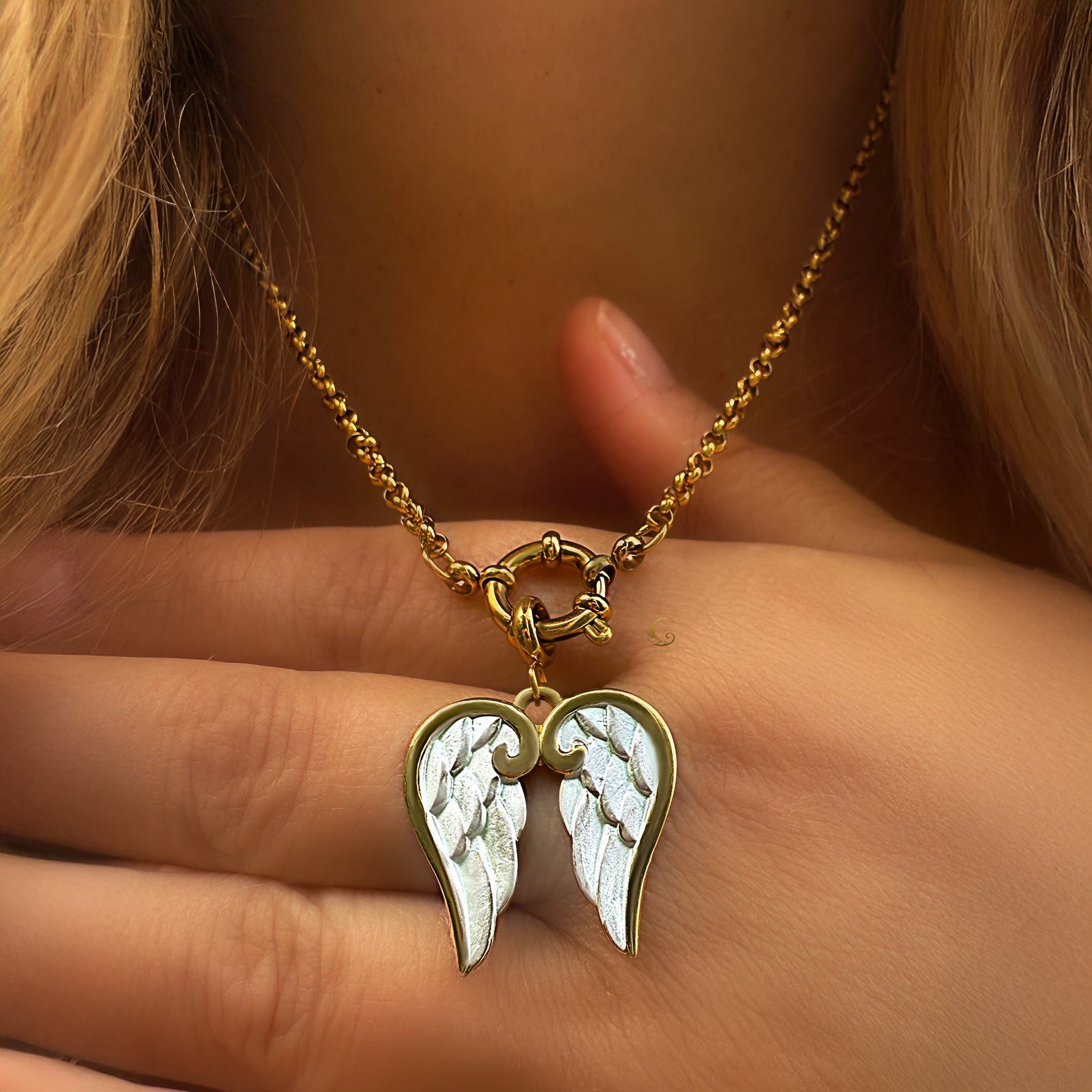 Gold necklace with a pendant shaped like angel wings held by a hand.