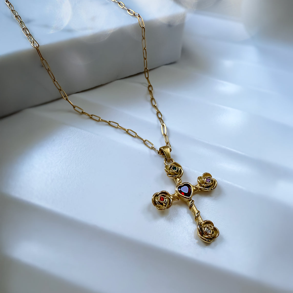 Gold cross necklace with a heart detail on a white surface