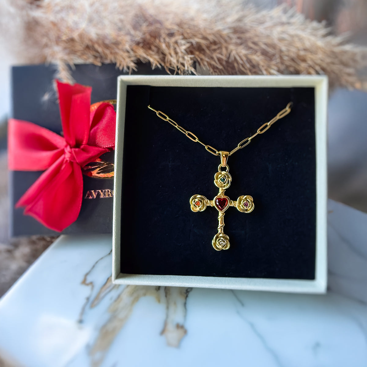Gold cross necklace with red gemstones in a box with a red bow in the background