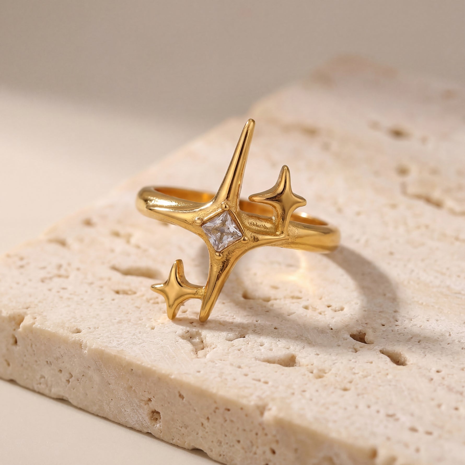 Gold ring with star designs on a textured beige surface