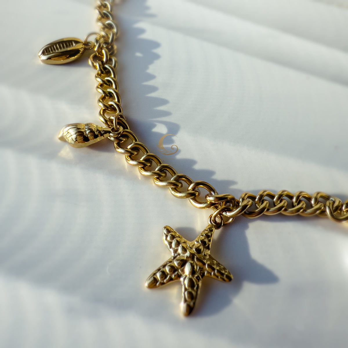 Close-up of textured starfish charm on Halina necklace, gold surface gleaming against stone backdrop