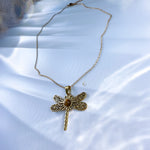 Gold dragonfly necklace with a gemstone on a white fabric background
