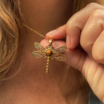 Gold dragonfly necklace being held near a person's neck