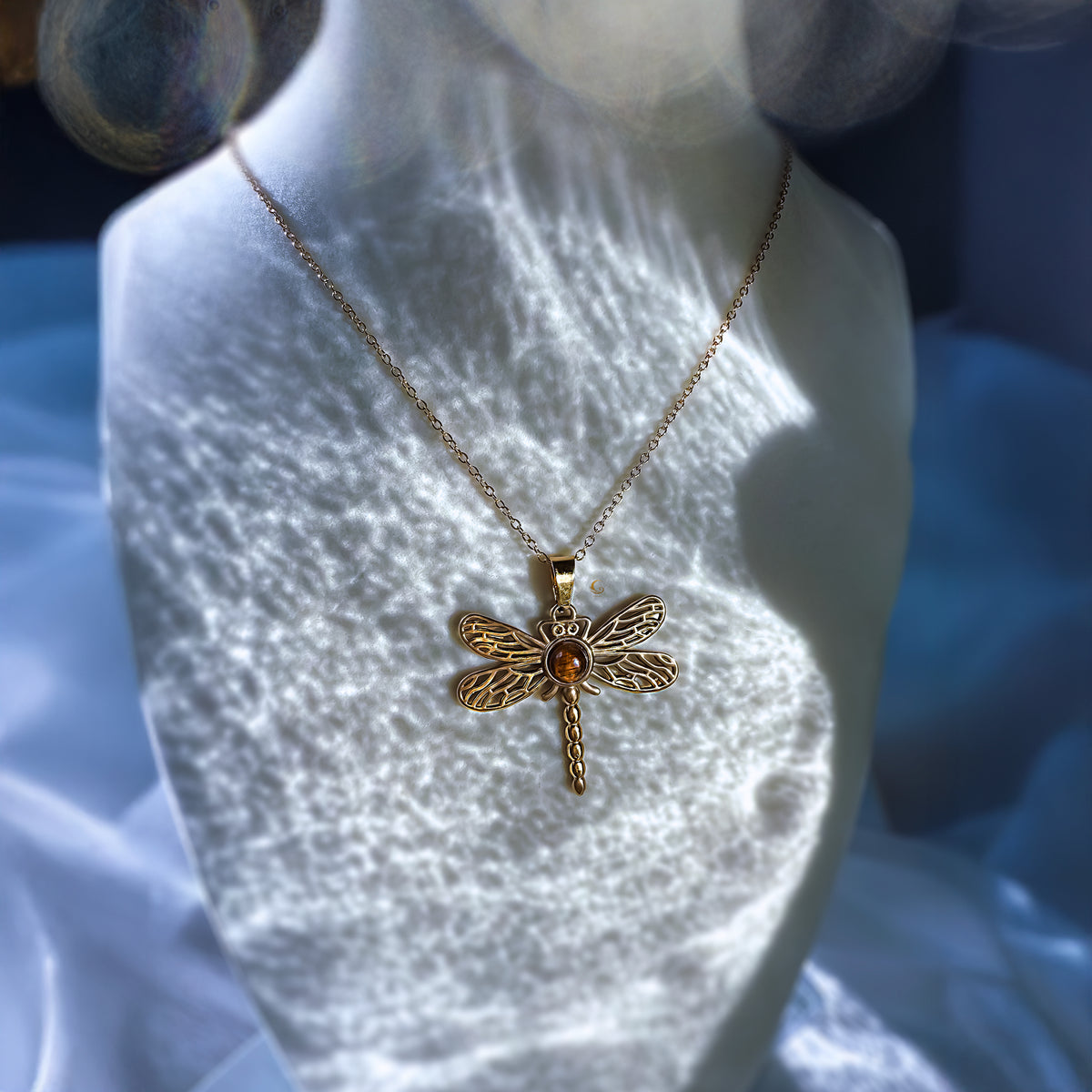 Gold dragonfly necklace on a mannequin bust with a blurred background