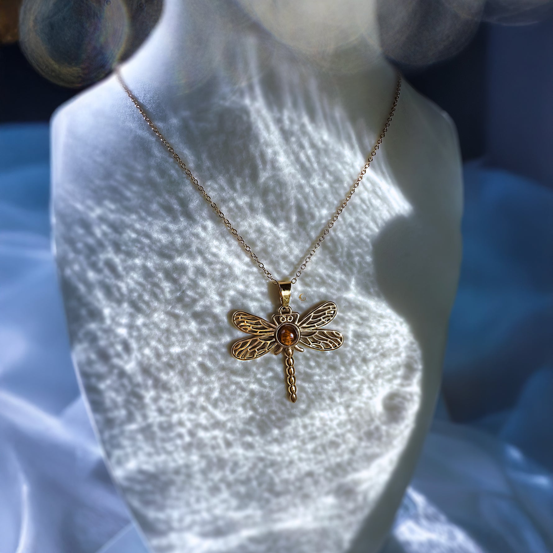 Gold dragonfly necklace on a mannequin bust with a blurred background