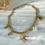 Complete gold charm necklace laid out with star, shells and vegan pearl on stone plate, glowing in warm light