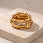Stack of gold rings with diamond accents on a textured beige surface