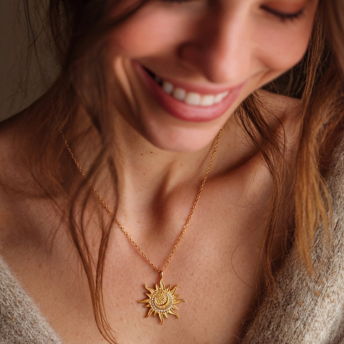 Woman wearing a gold necklace with a sun pendant, smiling.