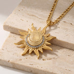 Gold sun-shaped necklace with embedded stones on a beige stone surface