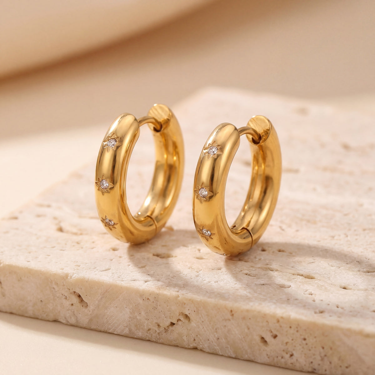 Gold hoop earrings with small diamonds on a beige stone surface