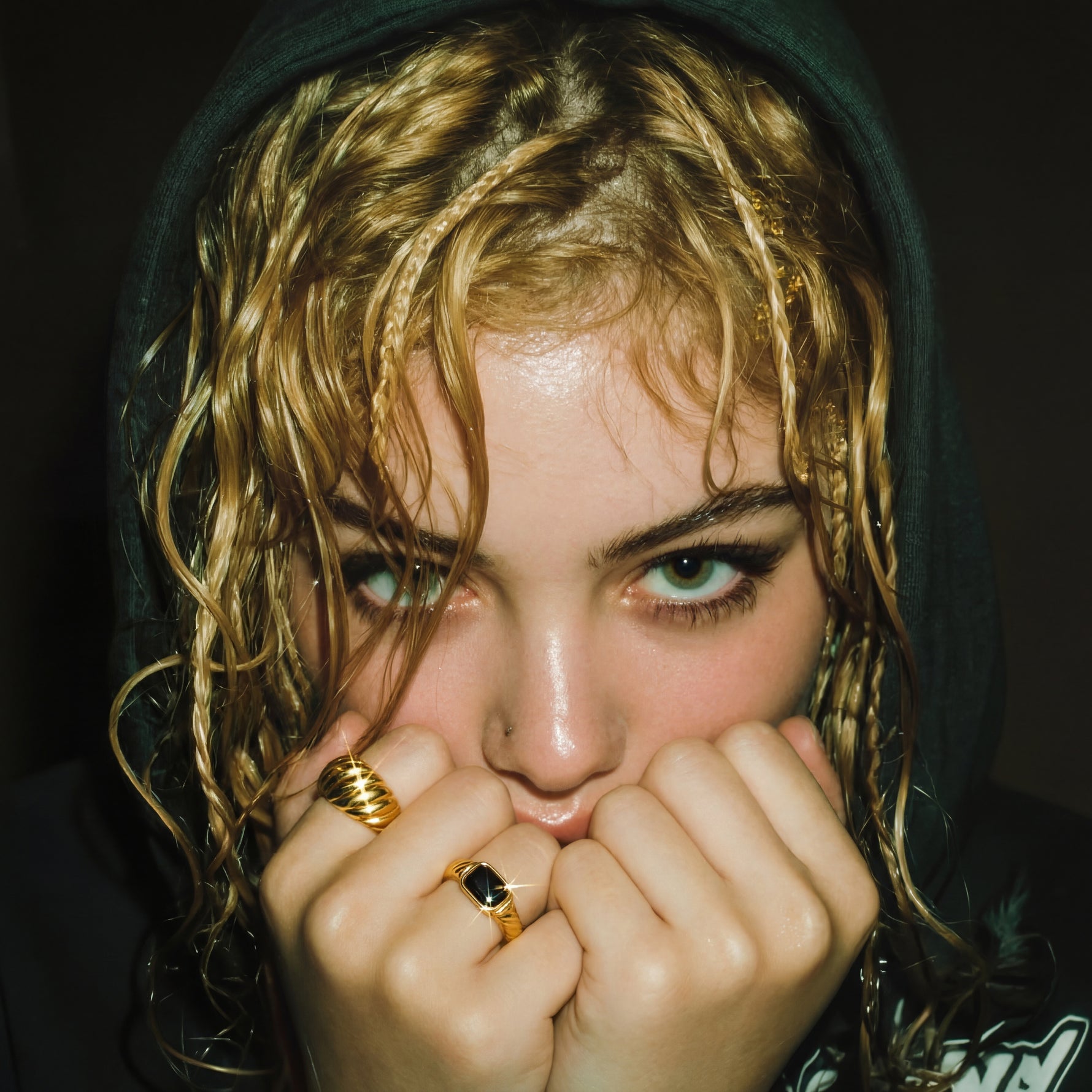 Person with wet hair wearing a dark hoodie, holding hands near face.