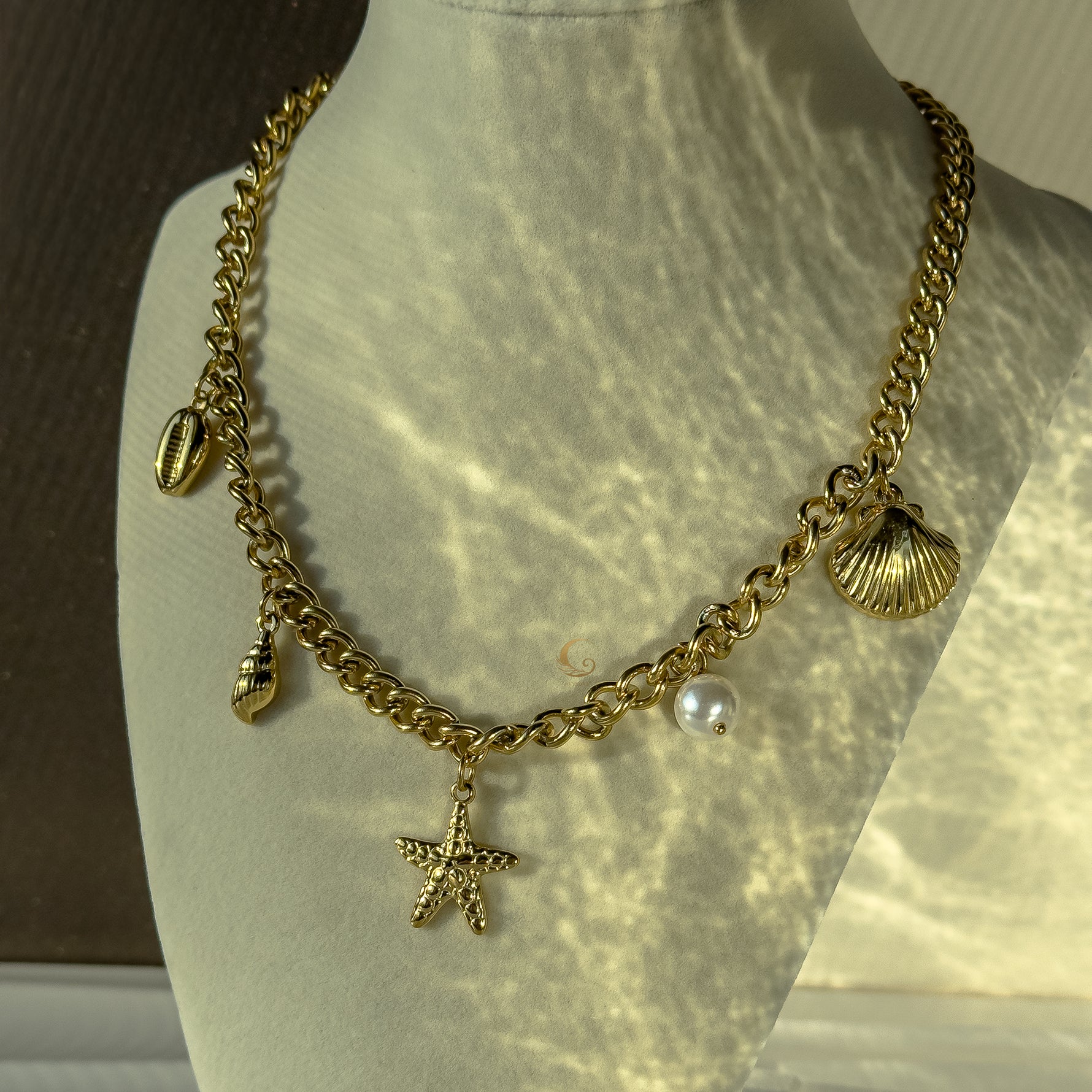 Halina necklace styled on mannequin bust, charms catching sunlight and casting soft reflections