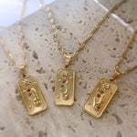 Three gold necklaces with tarot card-style pendants on a textured surface.