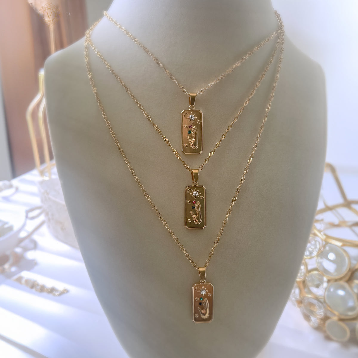 Three gold necklaces with rectangular pendants on a mannequin bust.