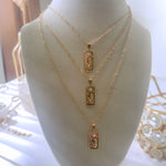 Three gold necklaces with rectangular pendants on a mannequin bust.