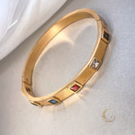 Bold gold bangle with vibrant red, clear, blue, and dark crystal accents, side view on neutral background – Fire Collection – Avyrona