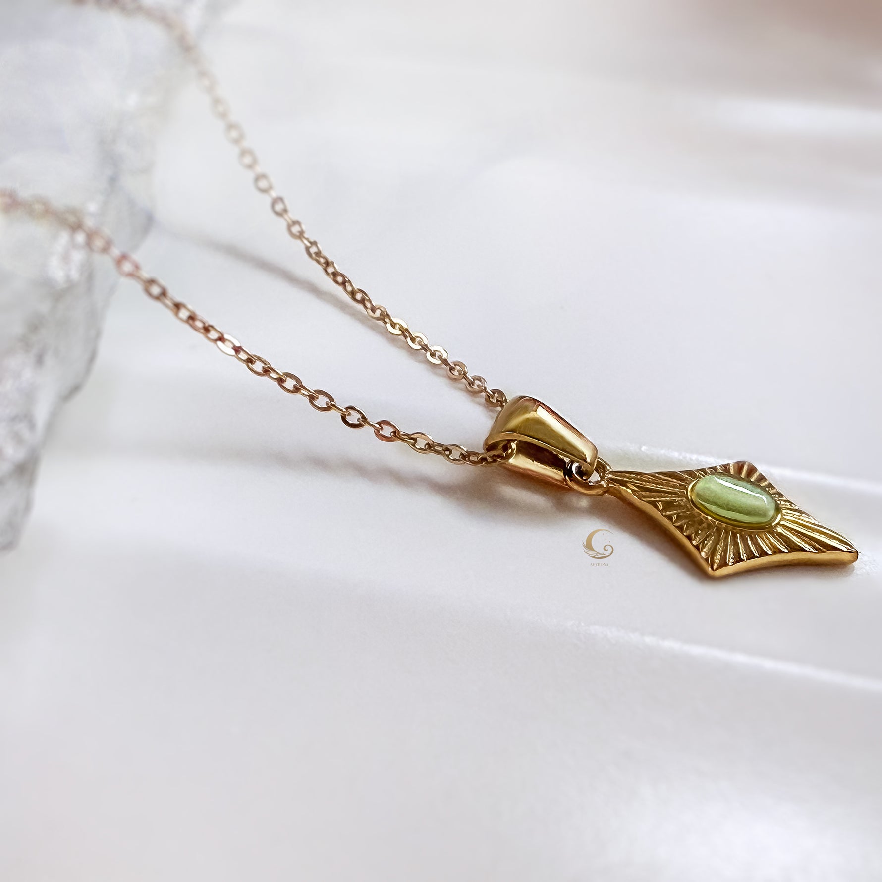 Side angle view of the Guardian Amulet necklace with green gemstone pendant on a soft satin background.