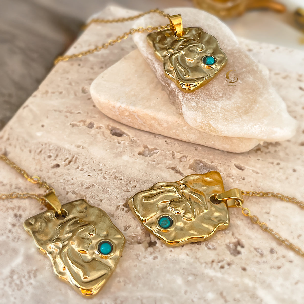 Gold necklaces with face-shaped pendants and turquoise stones on a stone surface