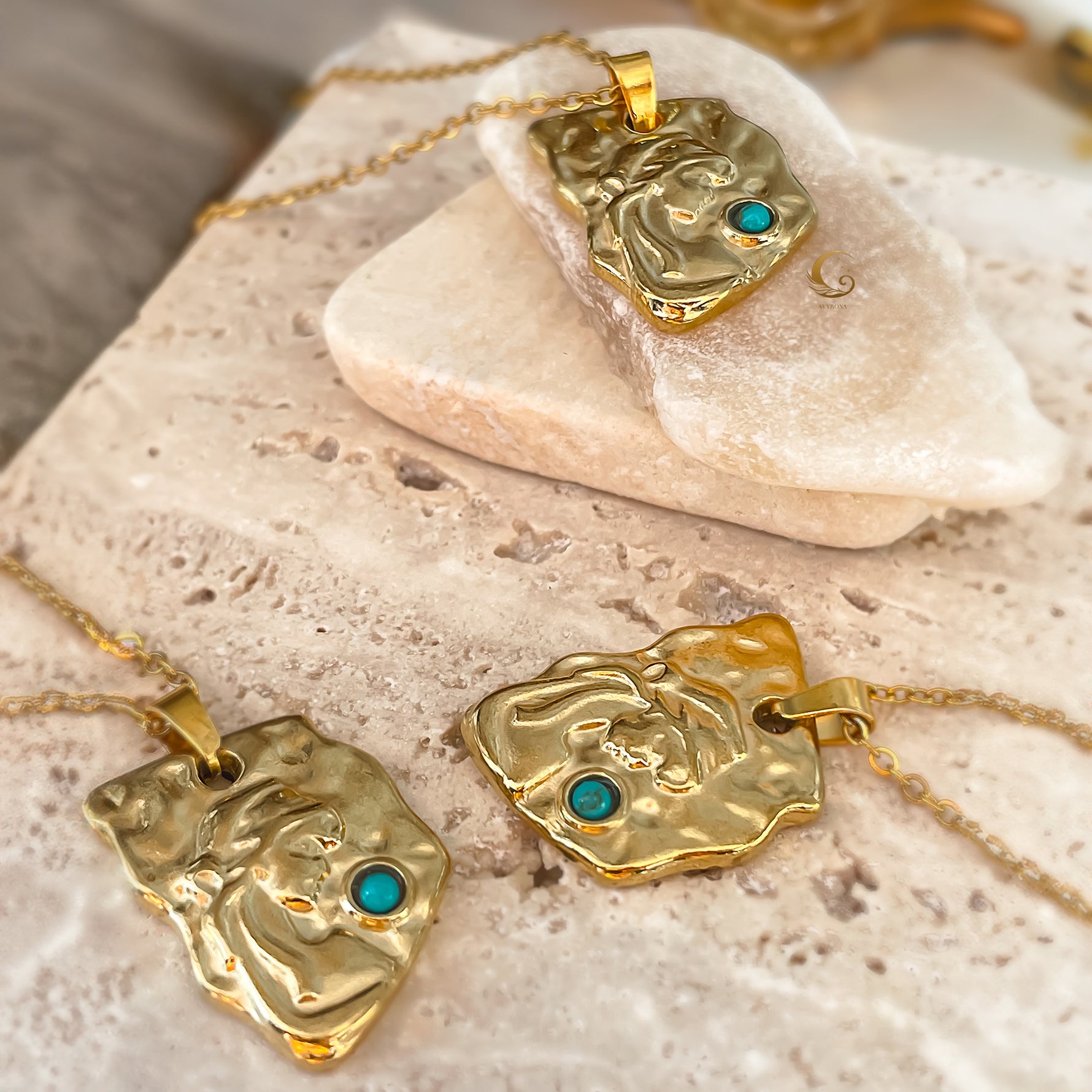 Gold necklaces with face-shaped pendants and turquoise stones on a stone surface