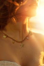 Woman wearing Halina necklace at sunset, ocean-inspired charms reflecting warm golden light on skin