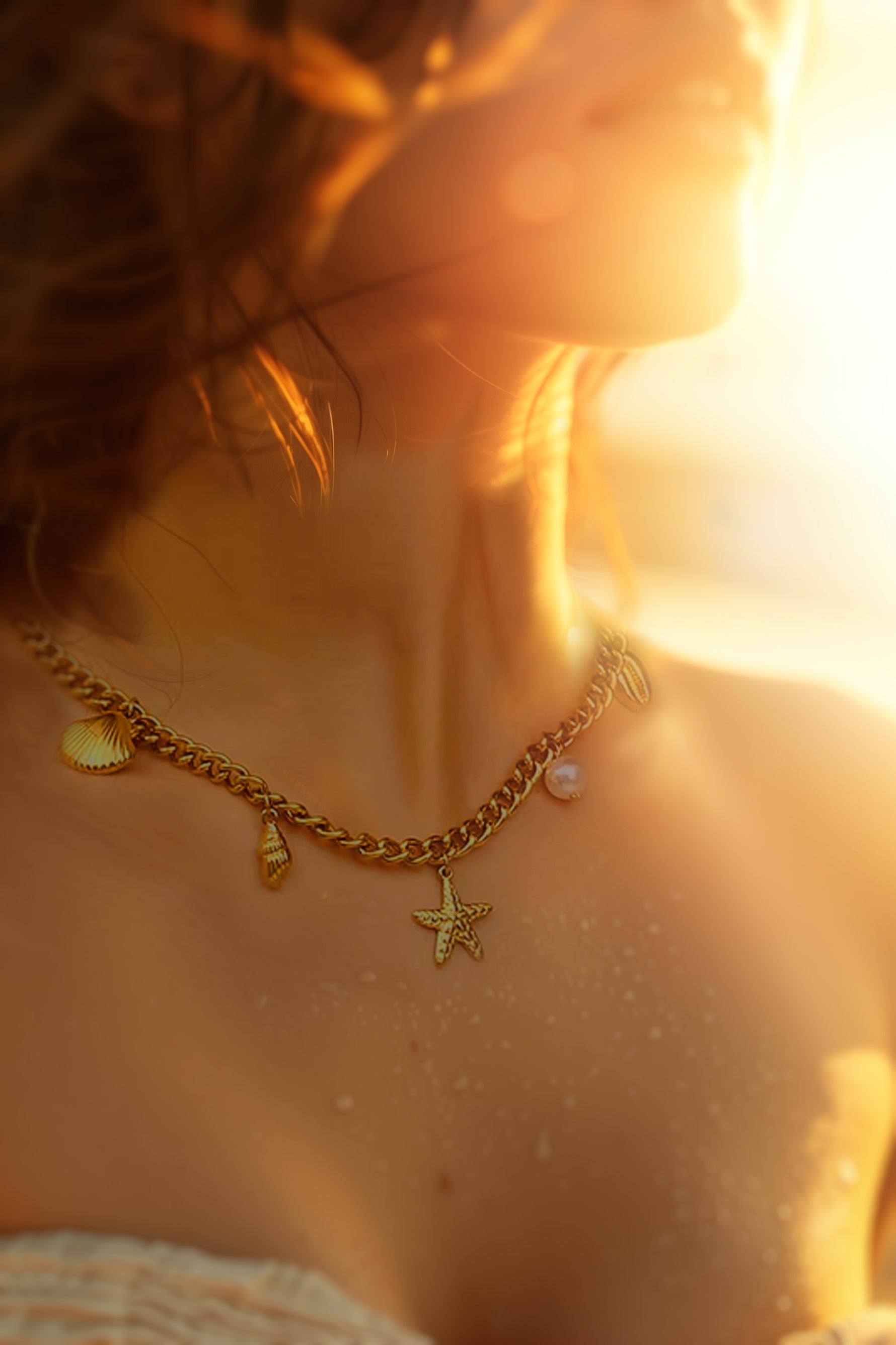 Woman wearing Halina necklace at sunset, ocean-inspired charms reflecting warm golden light on skin