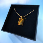 Gold necklace with a pendant on a black display box against a blue background