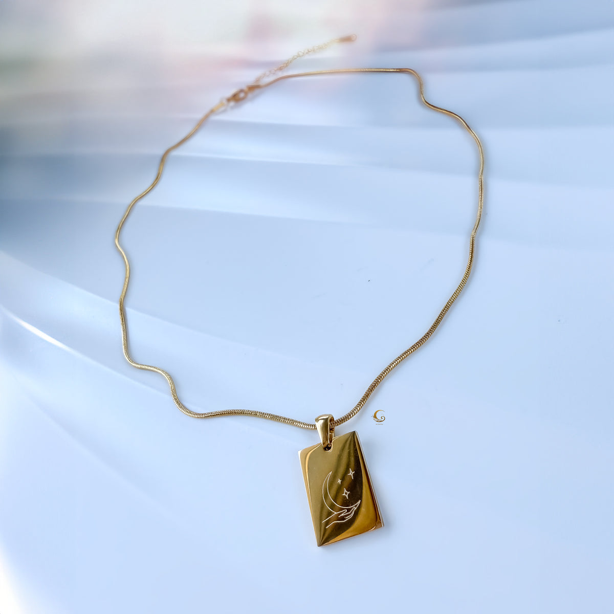Gold necklace with a leaf pendant on a light blue background