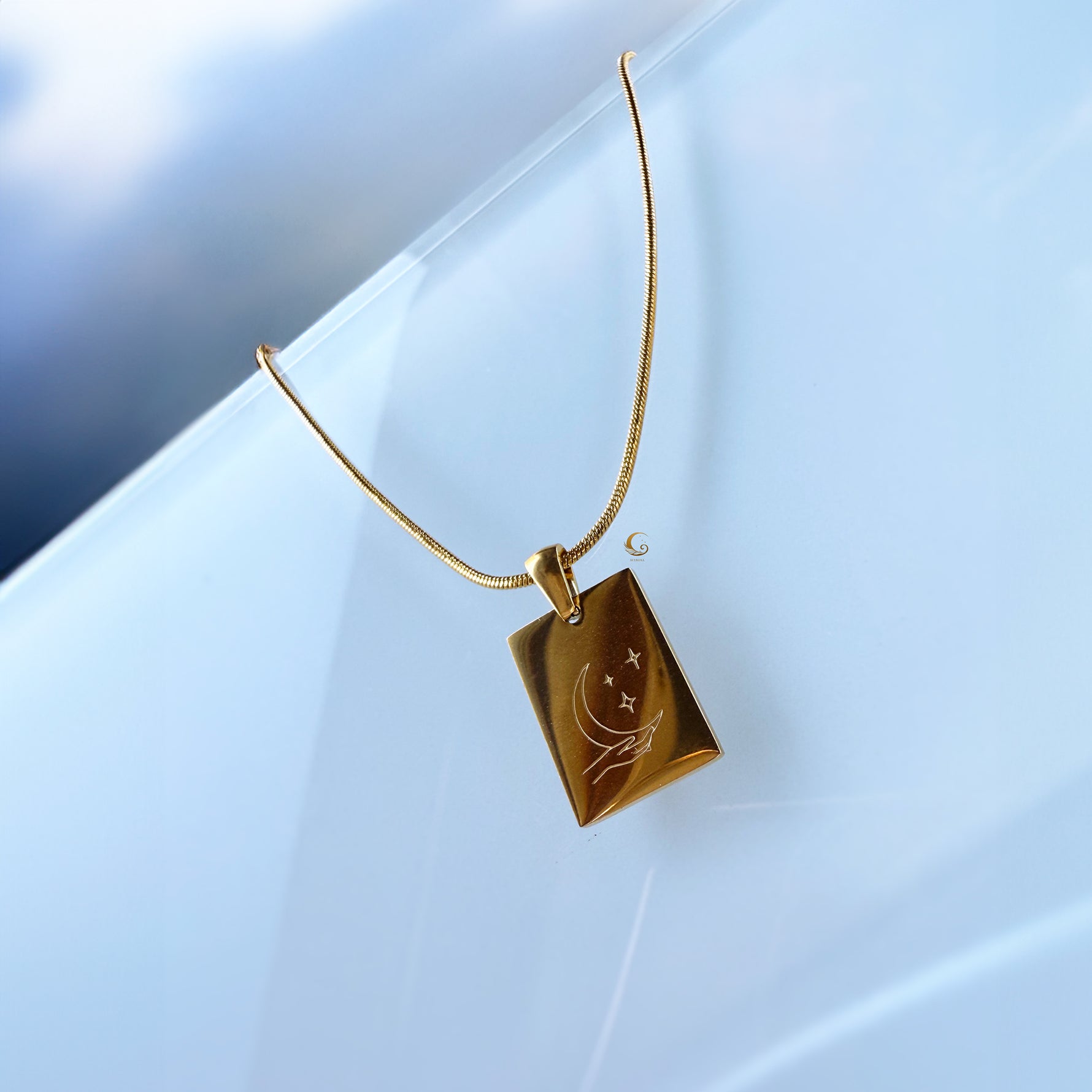 Gold necklace with a rectangular pendant on a light blue background