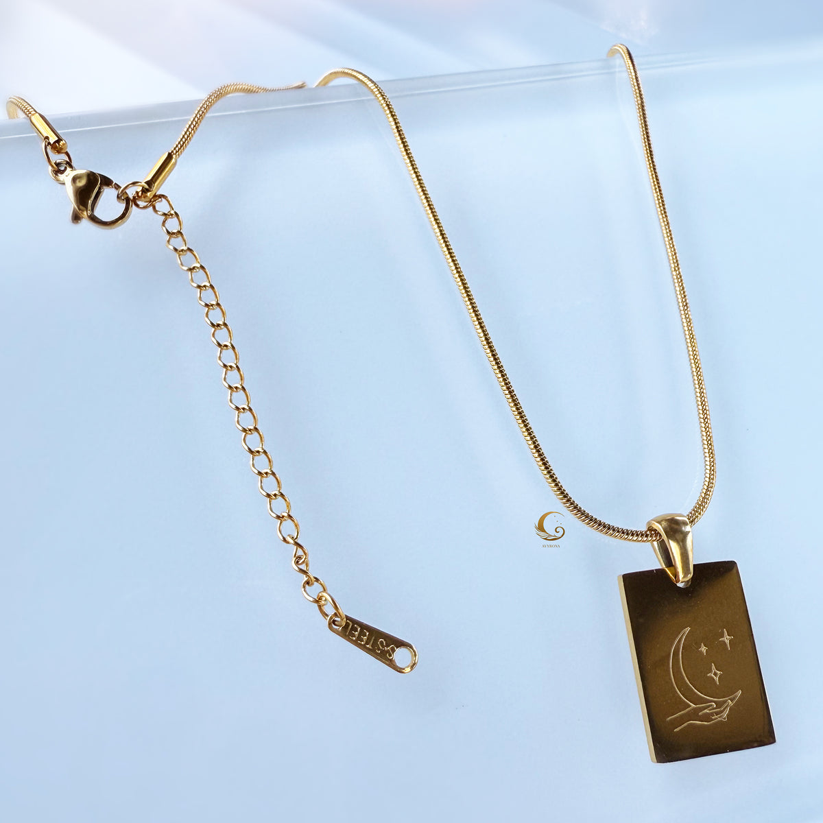 Gold necklace with a rectangular pendant on a light blue background