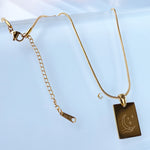 Gold necklace with a rectangular pendant on a light blue background