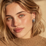 Close-up of a person with blonde hair wearing a brown sweater and earrings.