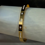 A gold bracelet adorned with a sun charm and sparkling cubic zirconia, displayed on a light-colored cylindrical stand.
