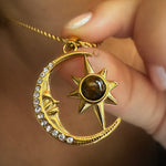 Gold necklace with moon and sun pendant held by a hand against a blurred background