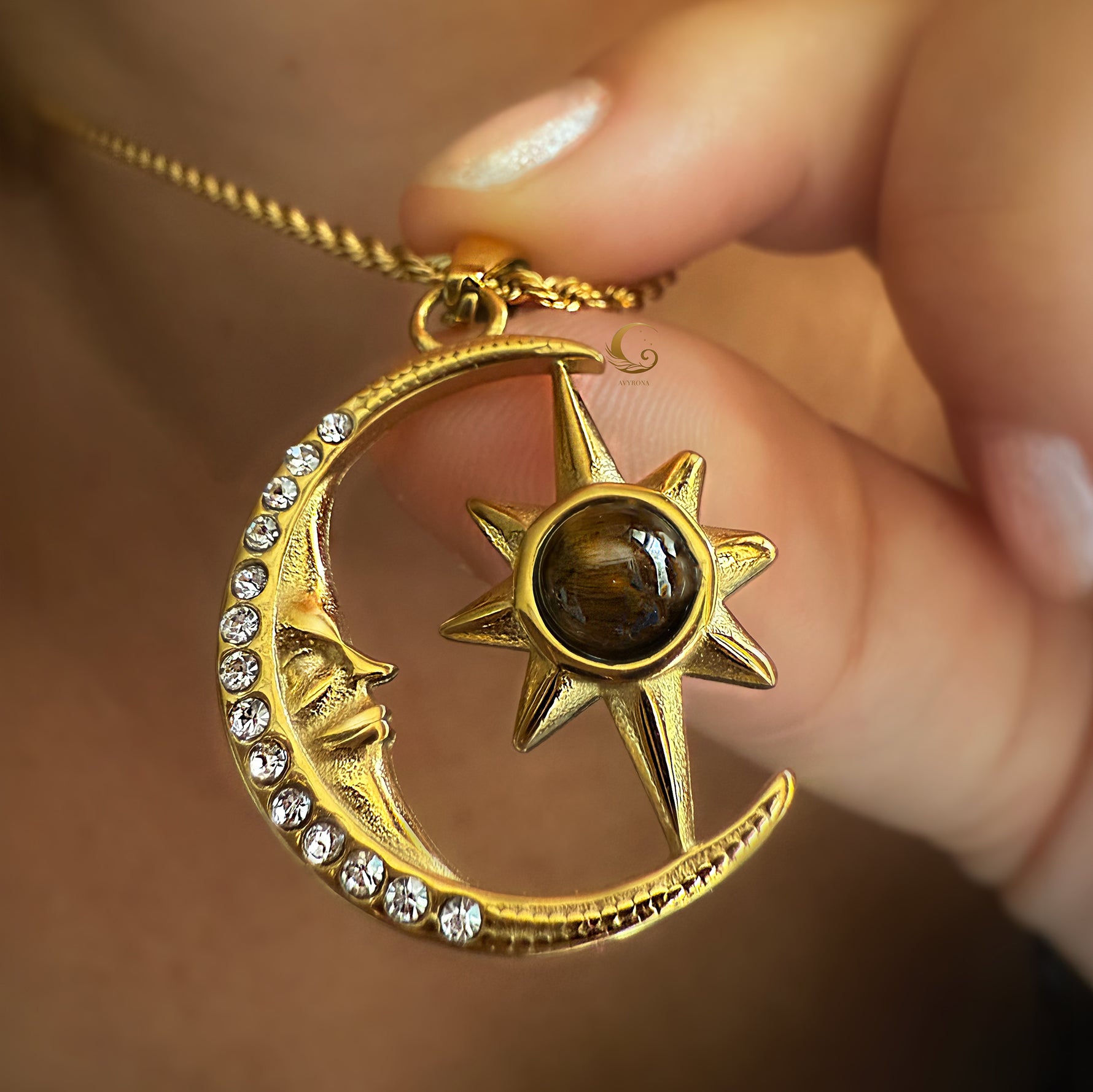 Gold necklace with moon and sun pendant held by a hand against a blurred background
