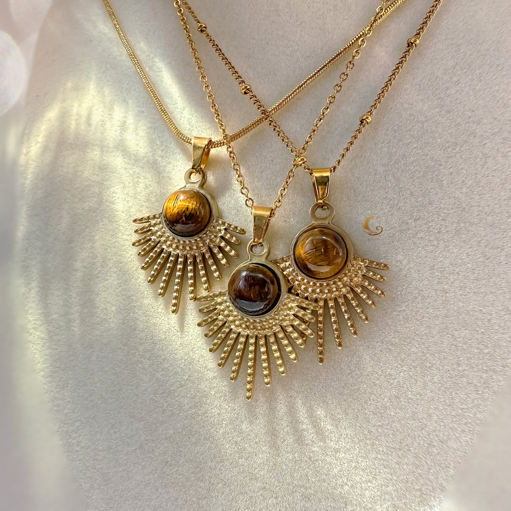 Three gold necklaces with sunburst pendants on a light background
