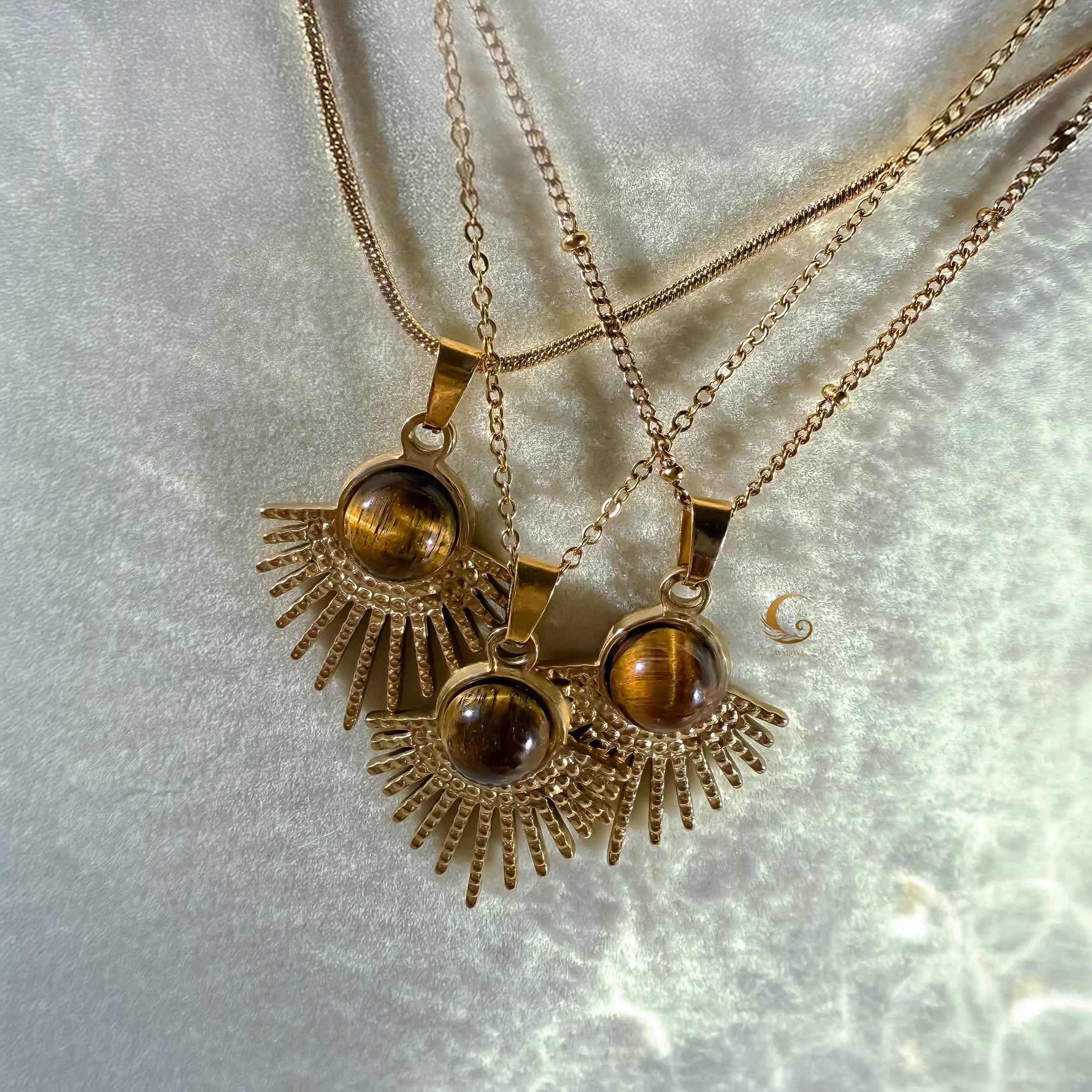 Three gold necklaces with tiger's eye pendants on a light gray background
