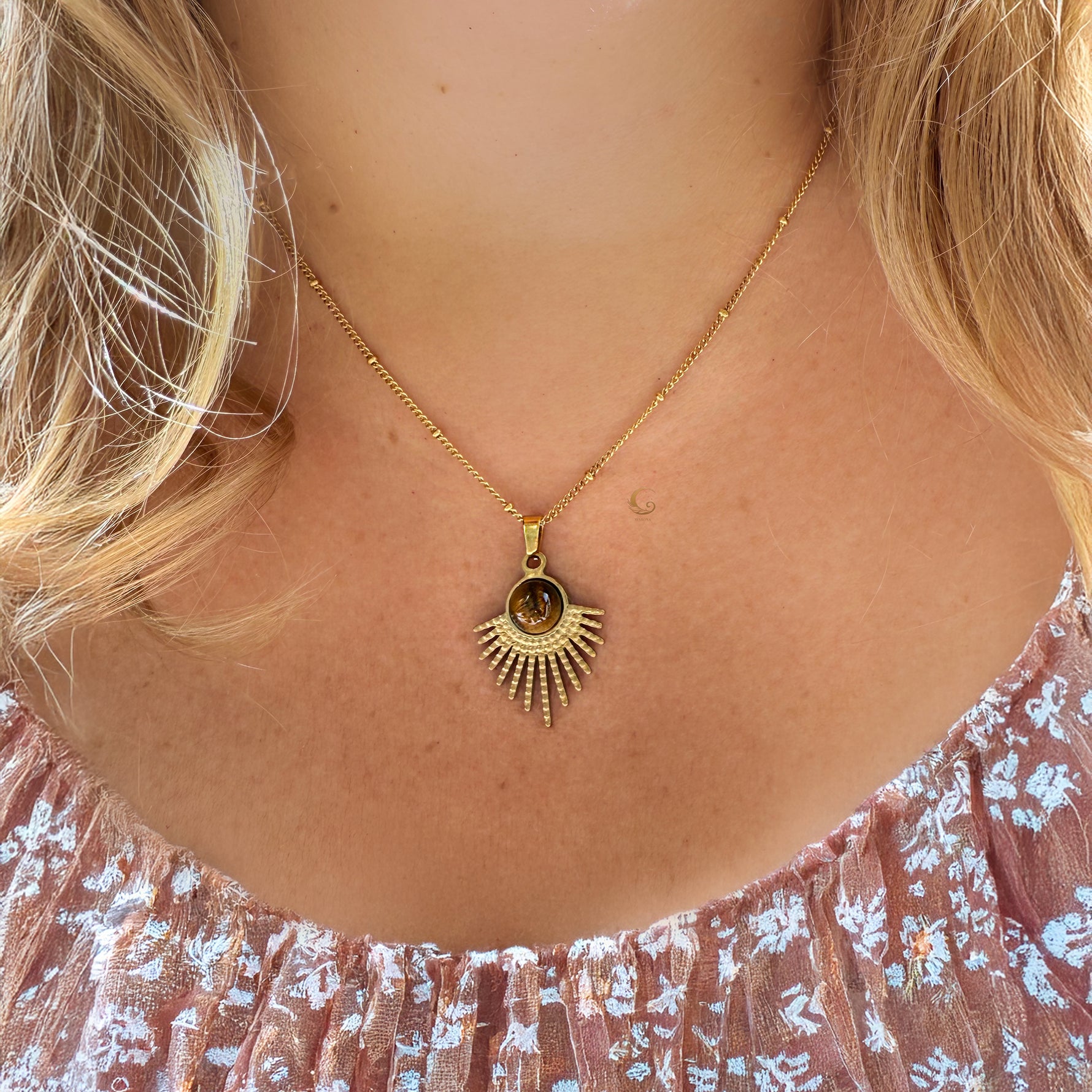 Gold necklace with a sunflower pendant worn by a person with blonde hair.