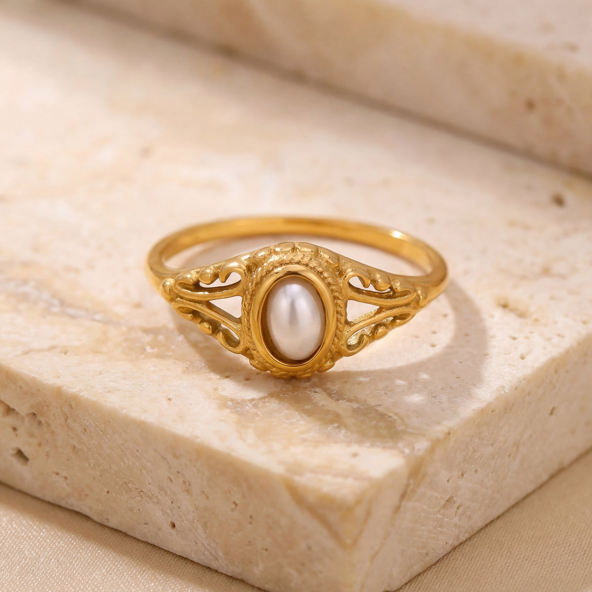 Gold ring with a pearl on a beige stone surface