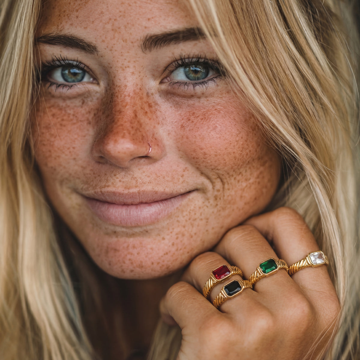 Close-up of a woman with freckles wearing multiple rings on her hand.