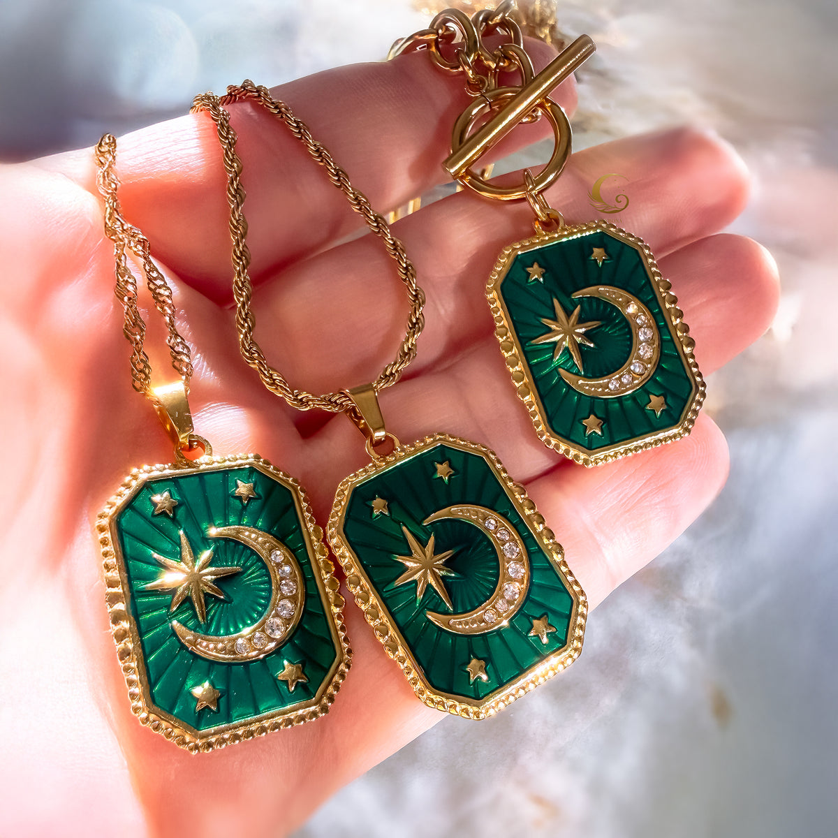 Green and gold jewelry set with pendants on a hand against a blurred background