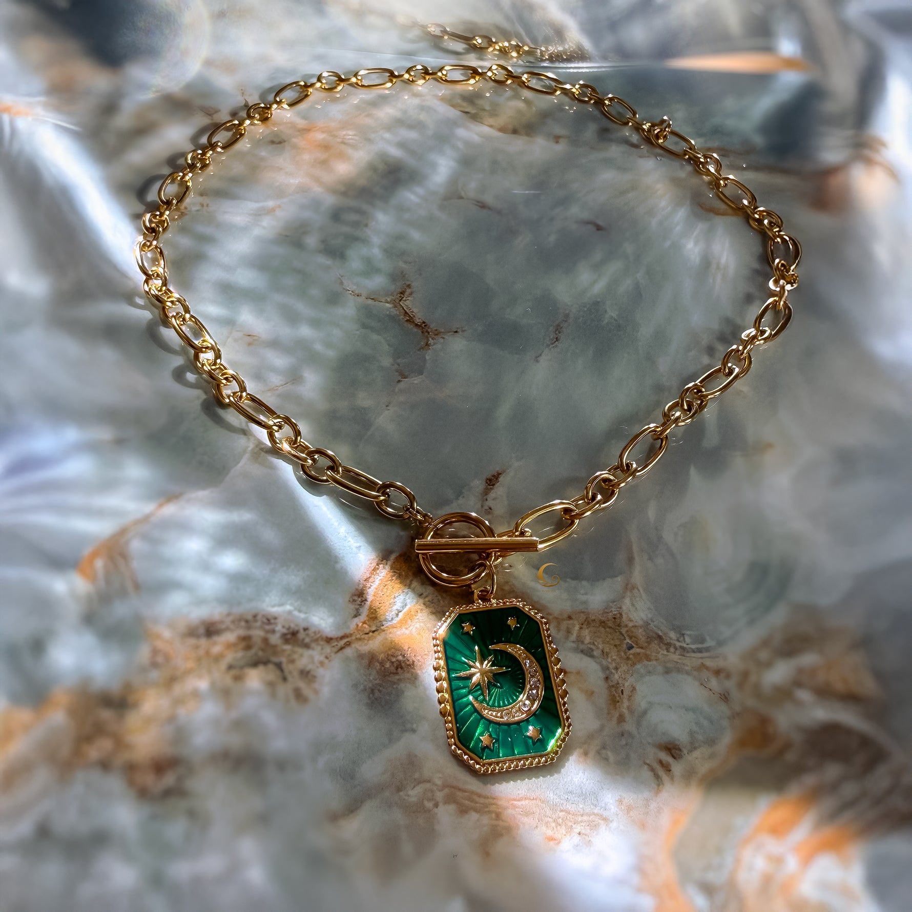 Gold bracelet with a green pendant on a marble surface