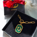 Gold and green pendant with a red bow on an Avyrona box