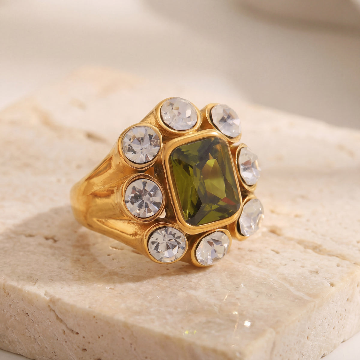 Gold ring with a green gemstone and clear stones on a beige stone surface