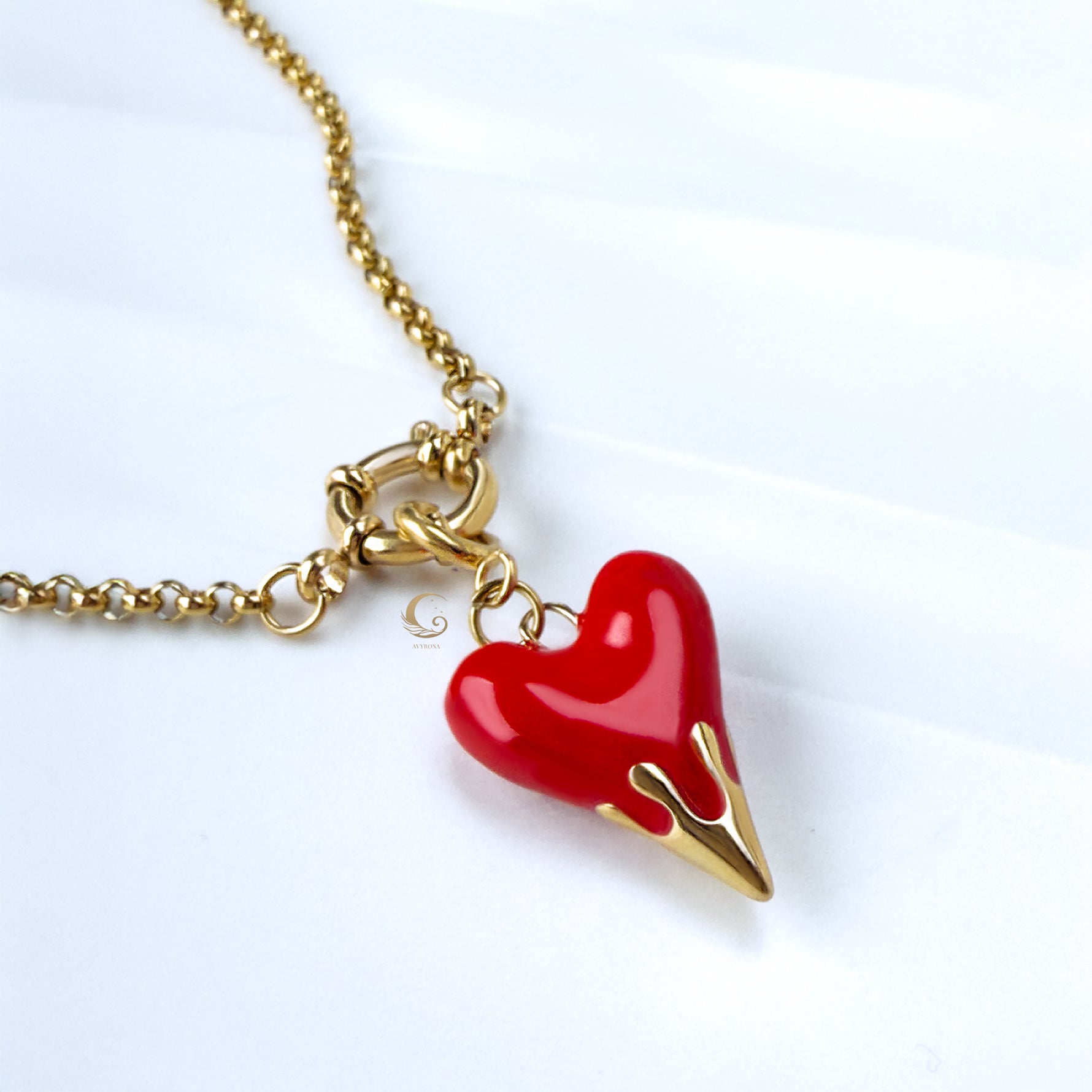 Close-up of red heart pendant with gold flame tip on chunky gold rolo chain, lying on marble-textured background