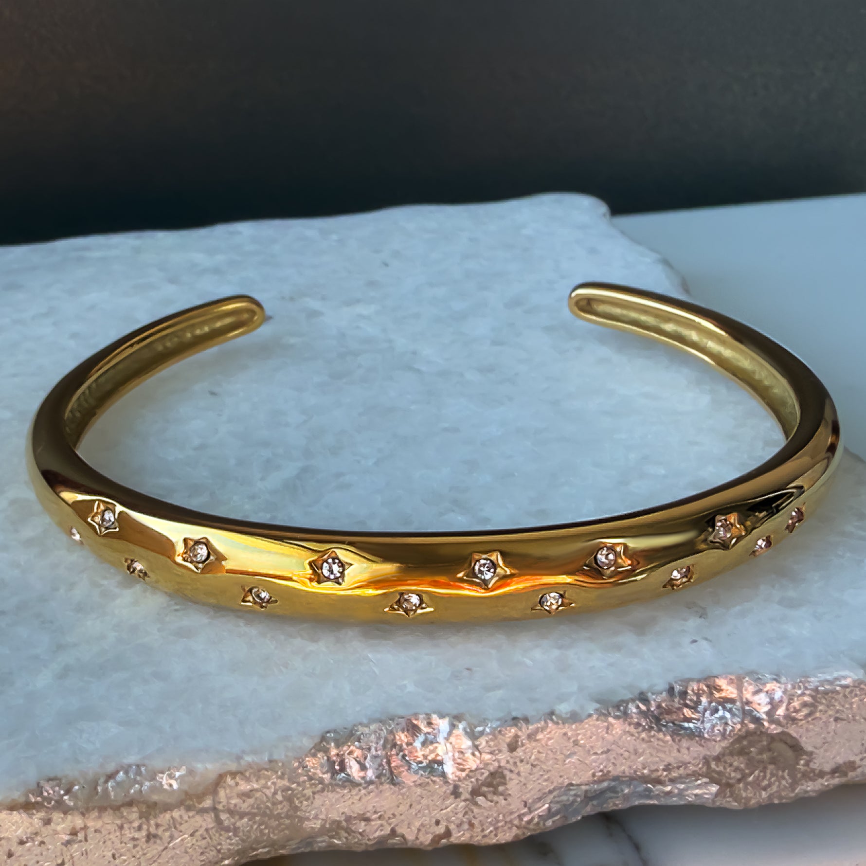 Aerina bracelet with clear zircon stars, resting on textured stone background.