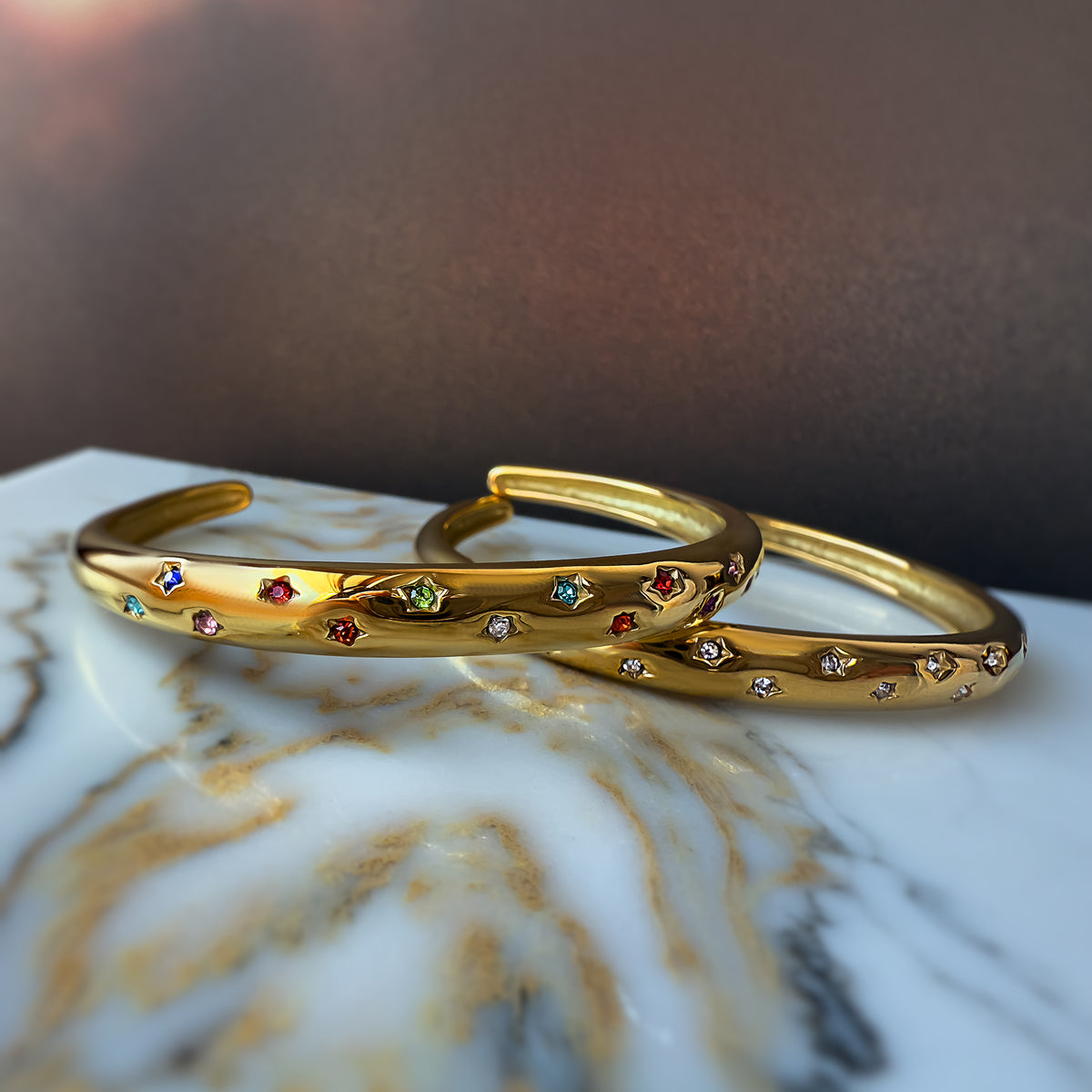 Flatlay of two Aerina bracelets – rainbow and clear versions – arranged on marbled background.